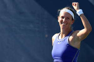 女網球運動員在藍色球場上微笑並舉起拳頭慶祝勝利。 — 網球 壁紙