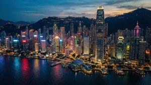 黃昏時分的香港天際線，燈火通明的摩天大樓倒映在港口水面上。