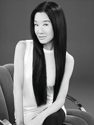 一位長黑髮的女士在黑白工作室肖像中，平靜地坐在一張現代椅子上。