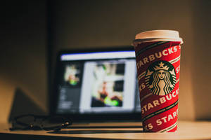 溫暖光線下，桌上一個紅色Starbucks咖啡杯，旁邊有手提電腦和眼鏡。 — 星巴克 壁紙