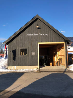 深色木製啤酒廠建築，地面有雪，天空清澈湛藍。