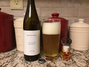 廚房檯面上的一瓶啤酒和一個玻璃杯，背景有紅色和白色的罐子。