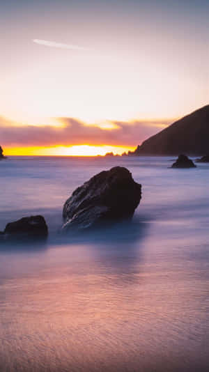 海洋上的夕陽，平滑的水和懸崖附近的深色岩石