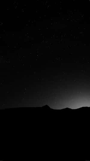 黑暗的山脈輪廓在繁星點點的夜空下，地平線上有微弱的光芒。