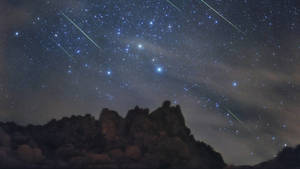 流星在夜間劃過岩石山脈上方的星空。 — 天空美學 壁紙