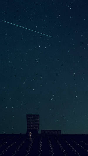 一顆流星劃過繁星點點的夜空，位於瓦片屋頂和磚砌煙囪上方。 — 天空美學 壁紙