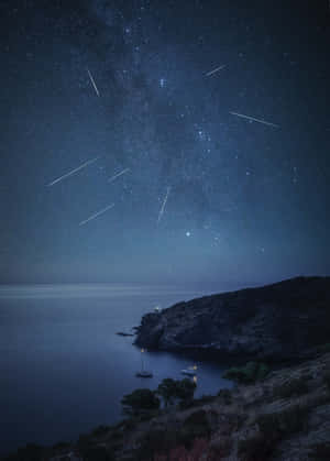 流星劃過繁星點點的夜空，下方是平靜的海面和岩石海岸，點亮的船隻點綴其間。 — Oppo Pad 5 壁紙