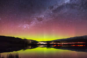 湖面在群山剪影下倒映著綠色極光和星空。 — 夜空 壁紙