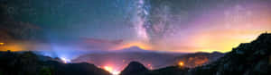 星空下的山脈，帶有發光的幾何圖案和遠處的燈光。 — 3840x1080 壁紙