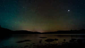 繁星之夜，北極光映照平靜的湖面和黑暗的山丘。 — 夜空 壁紙
