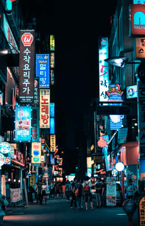 夜晚街景，有發光的霓虹招牌和行走的人們。 — Honor MagicPad4 壁紙