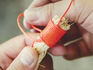 雙手將橙色繩索纏繞在一束天然纖維上。 — 4:3 壁紙