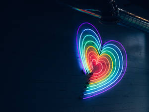 彩虹霓虹心臟在暗磚牆上發光，上方有工業管道。
