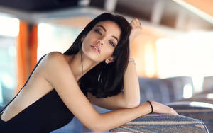 一位穿著黑色上衣的女性在現代室內空間中靠在一塊有圖案的表面上。