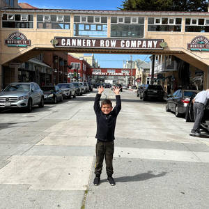 一個微笑的男孩舉起雙臂，站在Cannery Row拱門下的人行道上。 — 道路 壁紙