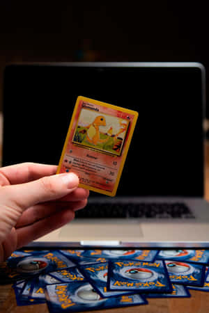 手拎住Glumanda Pokémon卡喺手提電腦上面，木枱上散落住精靈球卡。