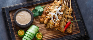 烤雞肉沙爹配花生醬、青瓜和青檸，放在木板上。