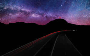 一條黑暗的道路在銀河可見的星空紫色天空下蜿蜒向山。 — 銀河系 壁紙