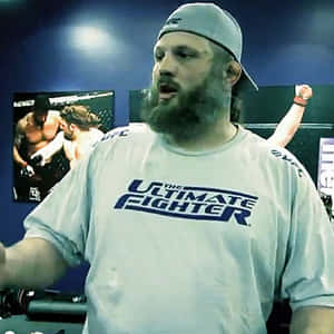 留鬍鬚的男子穿著UFC T恤在健身室中與搏擊海報一起做手勢。