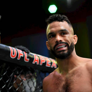 一位赤裸上身的MMA拳手在場館燈光下於UFC Apex八角籠內微笑。