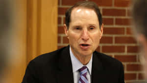 穿西裝打領帶的男子在室內磚牆附近說話 — 政治 壁紙