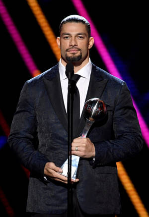 Roman Reigns 在彩色燈光下於舞台上手持 ESPY 獎項。