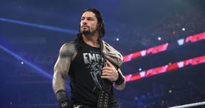 Roman Reigns 在摔角擂台上於場館燈光下手持冠軍腰帶。