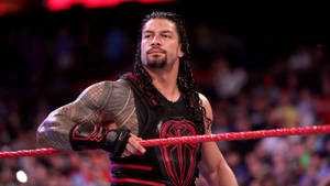 摔角手 Roman Reigns 在場館中緊握擂台繩索，身後有觀眾。