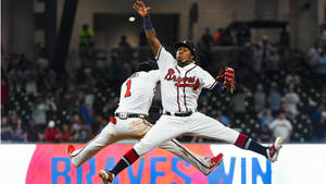 兩名棒球運動員在夜間比賽中跳躍慶祝，帶有「BRAVES WIN」標誌。