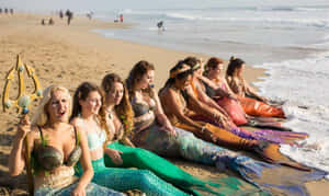 一群打扮成人魚的女性坐在海灘上，海浪拍打 — 美人魚 GIF 壁紙