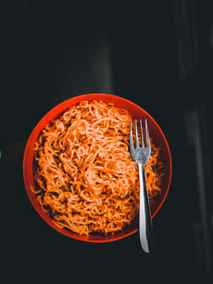 一個深色表面上的橙色即食麵碗，附有叉子。