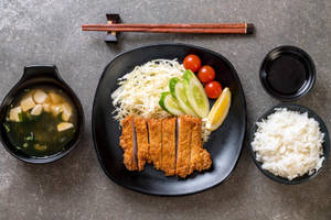 日式吉列豬排餐，配有白飯、味噌湯和蔬菜，盛載於深色碟上。 — 美食 壁紙