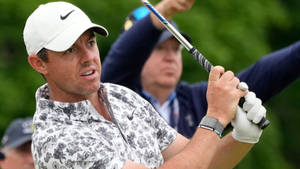 職業高爾夫球手 Rory McIlroy 揮桿中，身穿花卉圖案襯衫和白色帽子。 — 高爾夫 壁紙