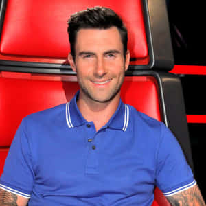 Adam Levine 身穿藍色Polo衫坐在紅色評審椅上微笑。 — 亞當·布羅迪 壁紙