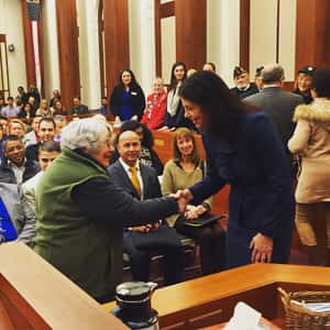一位身穿藍色西裝的女性在法庭內與一位年長男性握手。 — 政治 壁紙