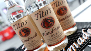 吧枱墊上嘅三支Tito's Handmade Vodka酒瓶，背景模糊。
