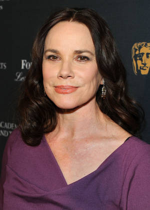 身穿紫色連衣裙的女性在BAFTA標誌背景的活動中微笑。 — 荷里活 GIF 壁紙