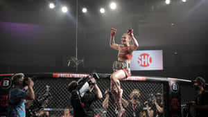 女性MMA拳手在攝影師包圍下跳上籠邊圍欄慶祝勝利。 — 超級英雄 壁紙