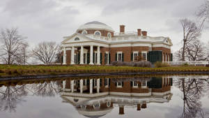 歷史悠久的大宅，帶有圓頂和柱子，倒映在平靜的池塘中，周圍是光禿的樹木。 — 雲朵 壁紙