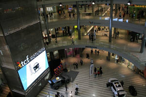 Multi-level shopping mall with shoppers and displayed cars.