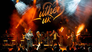 樂隊在明亮的燈光下於舞台表演，上方有「Luther UK」標誌。 — 星星 壁紙