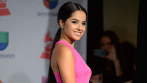 身穿粉色連衣裙的女性在紅地毯活動中微笑，背景有Univision和Grammy標誌。