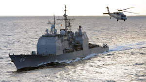 軍用驅逐艦在日落時分航行，直升機在海面上飛行。 — 直升機 壁紙