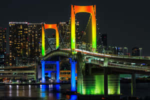 夜晚的東京彩虹橋被五彩燈光照亮，倒映在水面上。 — 3:2 壁紙