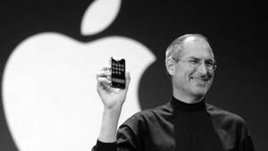 史提夫·喬布斯在舞台上展示第一部iPhone，身後有Apple標誌。