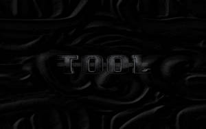 在黑暗漣漪布料背景上顯示「TOOL」的金屬文字。