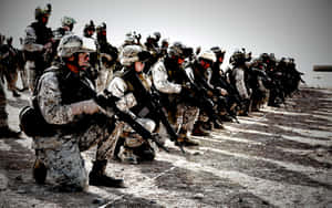 一排穿著沙漠裝備的武裝士兵跪在沙地上。 — 軍事動圖 壁紙