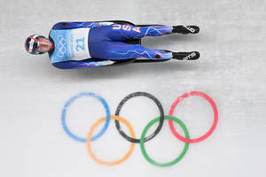 身穿美國隊服的雪橇運動員在冰道上飛馳，帶有奧運五環。 — 運動 壁紙