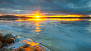 日落時分的冰凍湖泊，金色光線在冰面和積雪岩石上。 — 寒冷 壁紙