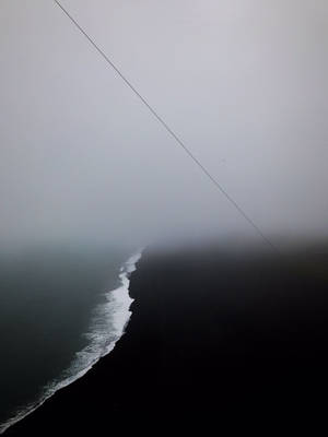 一個霧氣瀰漫的海岸場景，黑暗的海灘和海洋波浪在灰色天空下，帶有對角線纜繩。